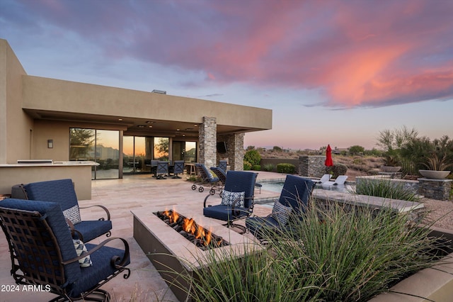 patio terrace at dusk featuring an outdoor bar, a fire pit, and a pool