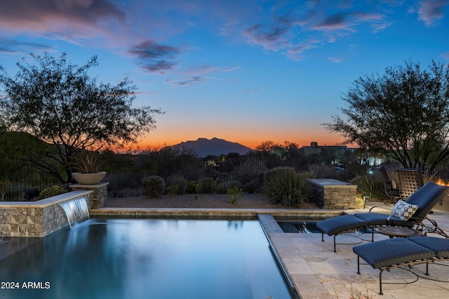 pool at dusk with a patio area, pool water feature, and a mountain view