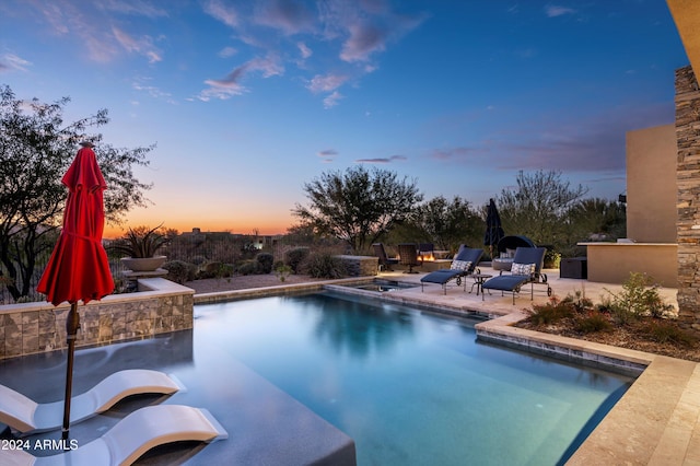 pool at dusk featuring a patio area and an outdoor stone fireplace