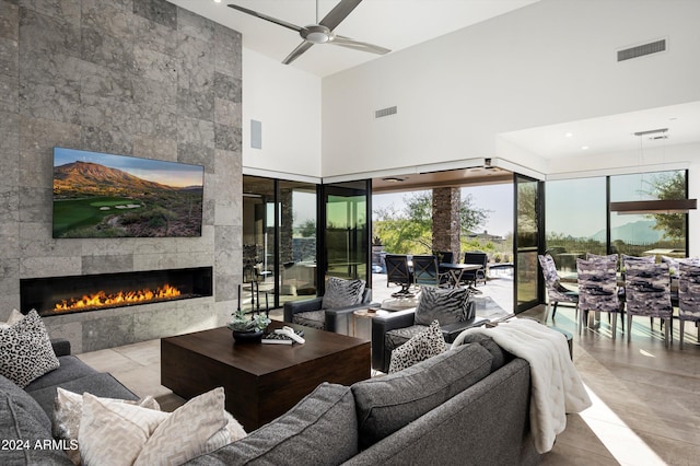 living room with ceiling fan, a fireplace, a towering ceiling, and light tile patterned floors