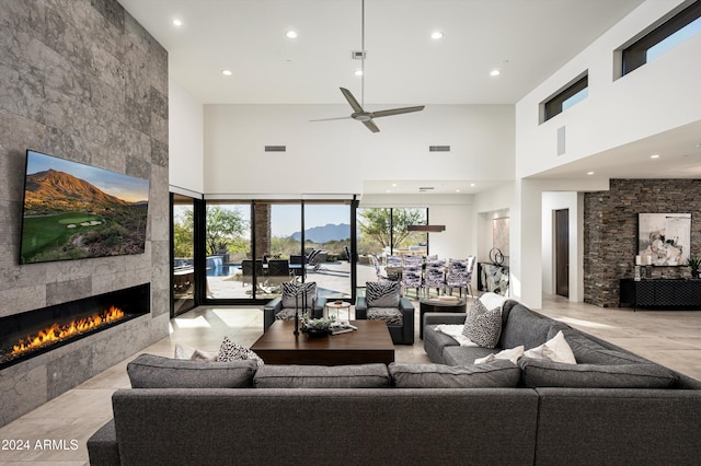 living room featuring a tiled fireplace, ceiling fan, and a high ceiling