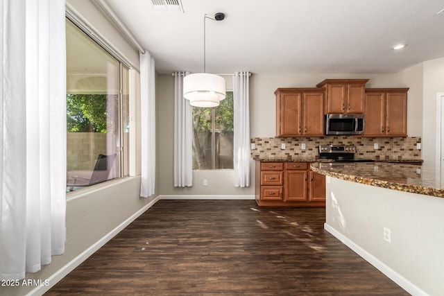 kitchen with appliances with stainless steel finishes, dark stone countertops, backsplash, dark hardwood / wood-style floors, and decorative light fixtures