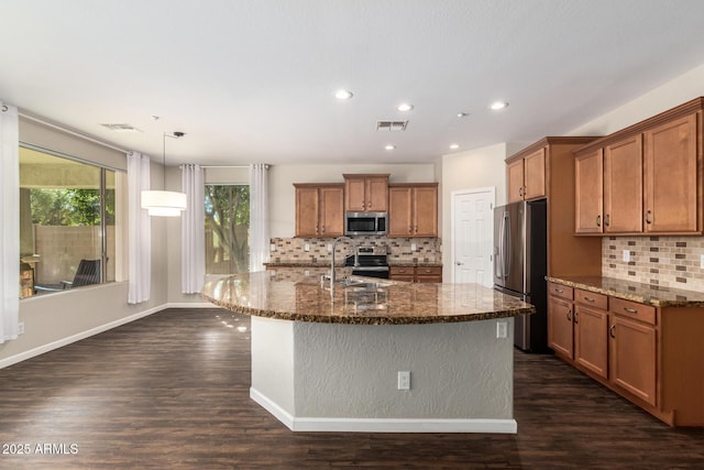 kitchen with an island with sink, appliances with stainless steel finishes, decorative light fixtures, and sink