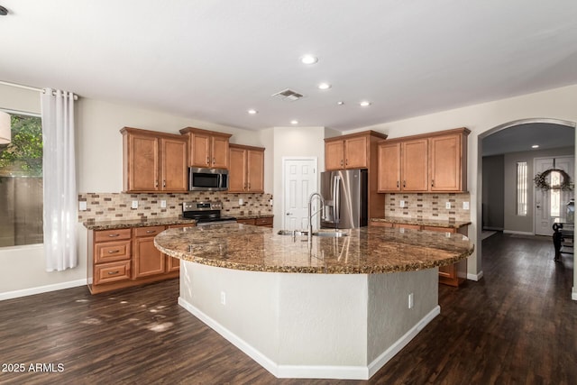 kitchen with sink, dark stone counters, dark hardwood / wood-style flooring, stainless steel appliances, and a kitchen island with sink