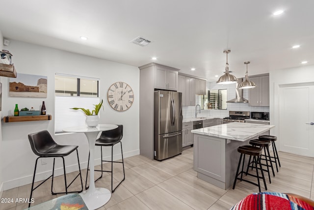 kitchen featuring gray cabinets, a kitchen island, sink, decorative backsplash, and appliances with stainless steel finishes