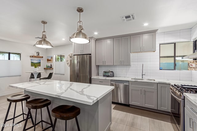 kitchen featuring a kitchen island, sink, hanging light fixtures, appliances with stainless steel finishes, and gray cabinets