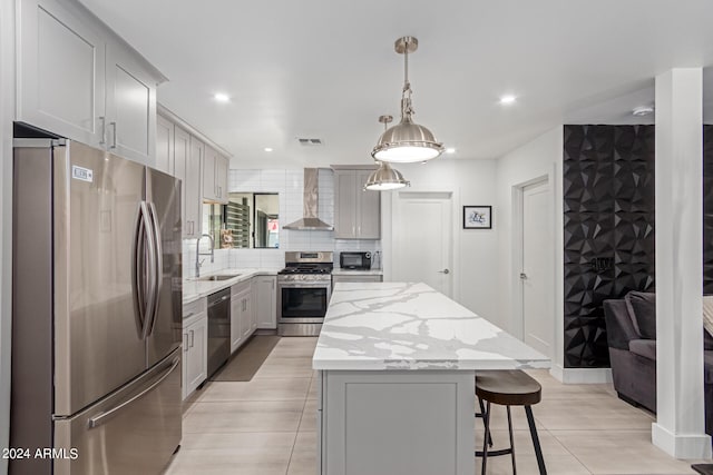 kitchen with sink, gray cabinetry, wall chimney range hood, stainless steel appliances, and a center island