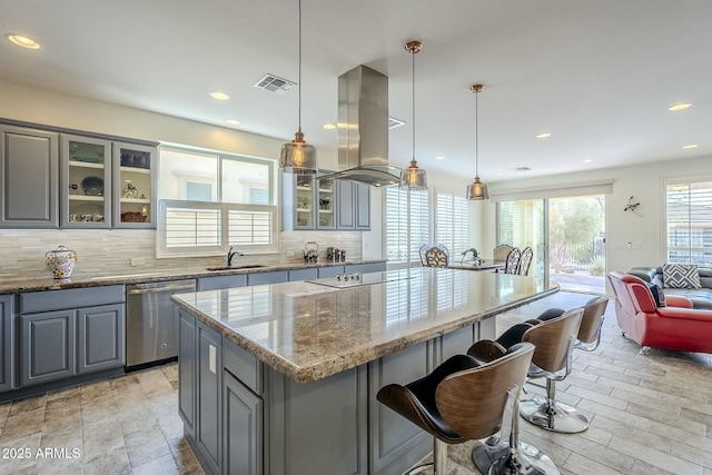 kitchen featuring gray cabinets, island range hood, dishwasher, hanging light fixtures, and light stone counters