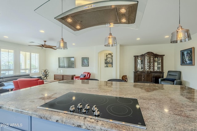 kitchen with ceiling fan, premium range hood, hanging light fixtures, light stone counters, and black electric cooktop