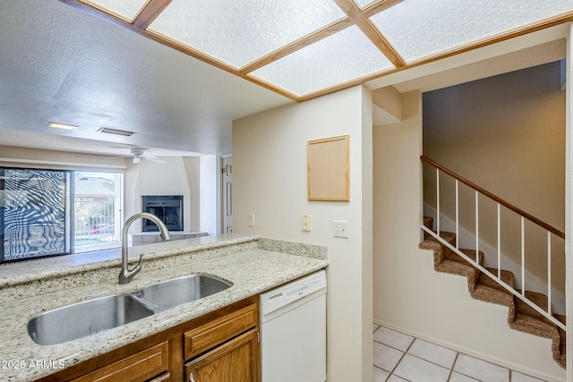 kitchen with sink, light tile patterned floors, dishwasher, ceiling fan, and light stone countertops