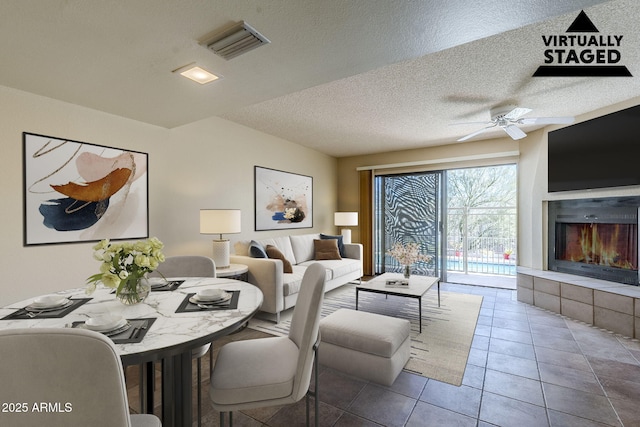 dining space with ceiling fan, tile patterned floors, a fireplace, and a textured ceiling