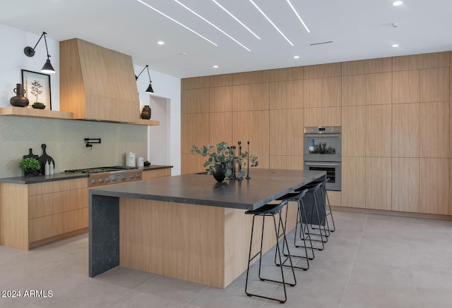 kitchen with a spacious island, light brown cabinetry, appliances with stainless steel finishes, custom range hood, and decorative backsplash