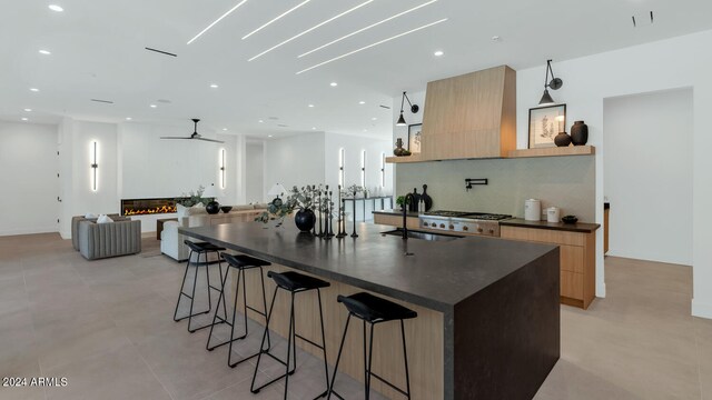 kitchen featuring sink, wall chimney range hood, a breakfast bar, ceiling fan, and a spacious island