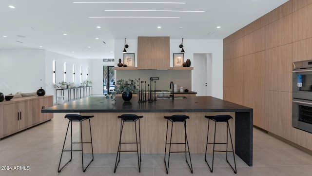 kitchen featuring a spacious island, a breakfast bar, sink, light brown cabinets, and stainless steel double oven