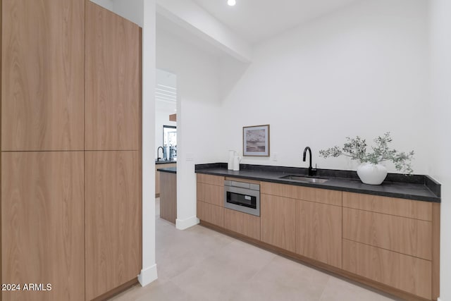 kitchen featuring sink, dark stone countertops, oven, and light brown cabinetry