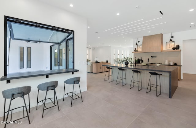 kitchen with sink, a kitchen bar, light tile patterned floors, kitchen peninsula, and light brown cabinets