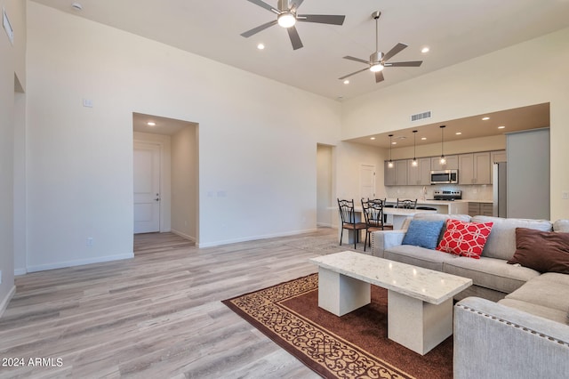 living room featuring a towering ceiling, ceiling fan, and light wood-type flooring