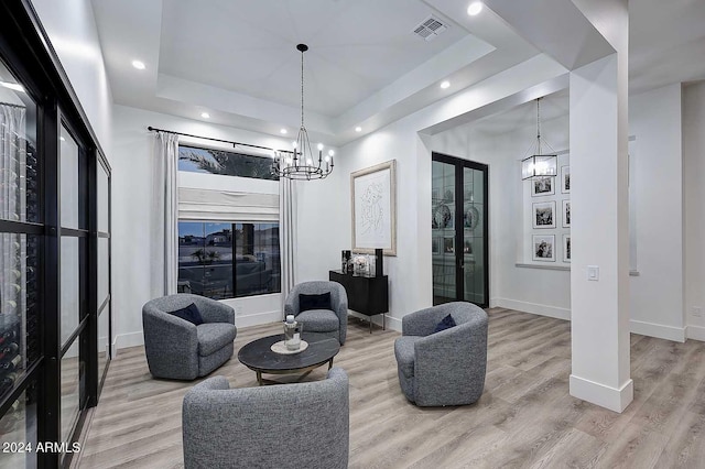 living room with light wood-type flooring, a raised ceiling, and a chandelier