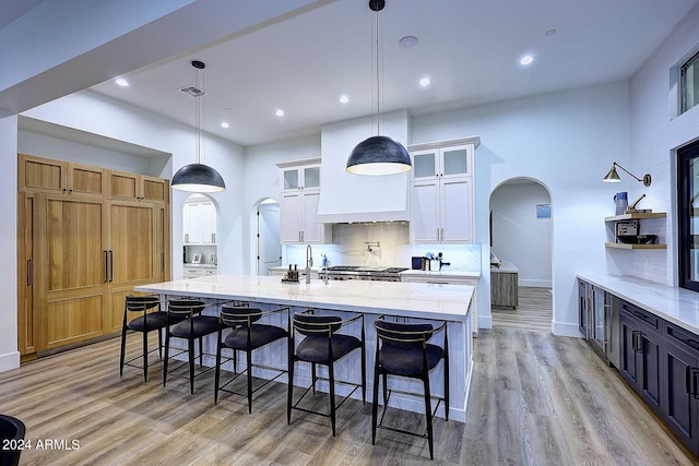 kitchen featuring white cabinetry, light stone counters, pendant lighting, light hardwood / wood-style flooring, and a spacious island