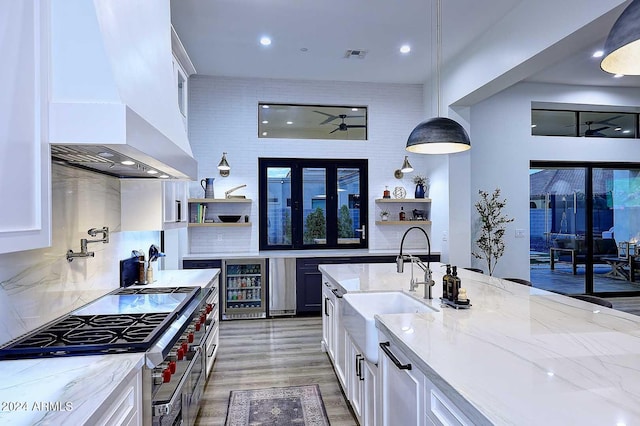 kitchen with light stone counters, white cabinets, wall chimney exhaust hood, pendant lighting, and beverage cooler