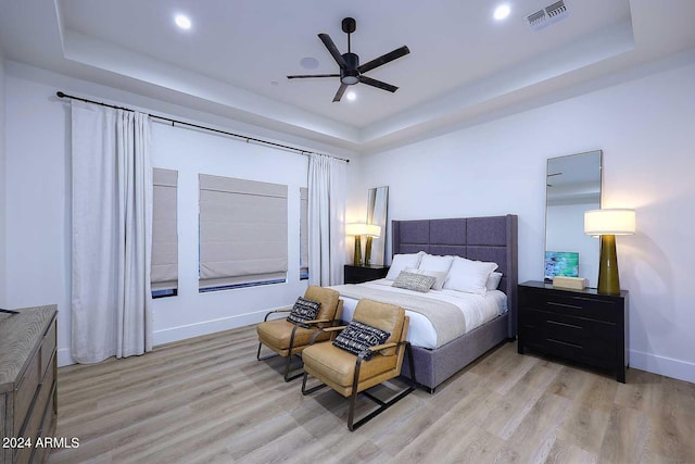 bedroom with light hardwood / wood-style floors, a tray ceiling, and ceiling fan