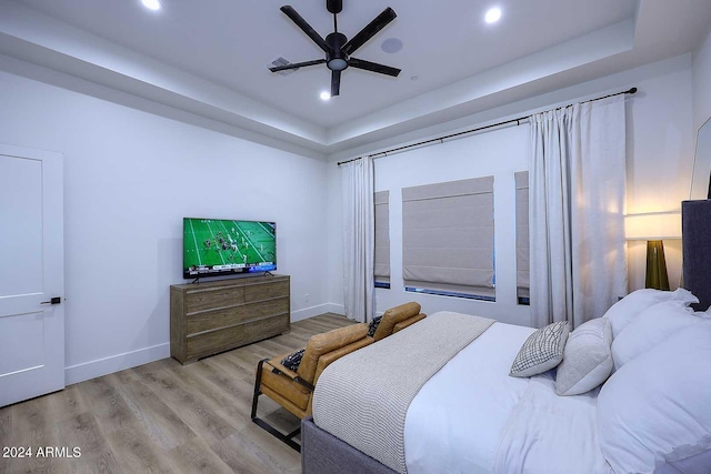 bedroom with light wood-type flooring, a raised ceiling, and ceiling fan