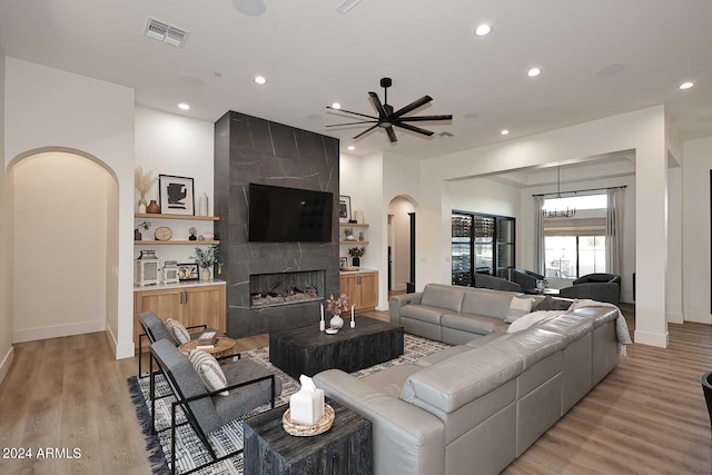 living room featuring ceiling fan with notable chandelier, light hardwood / wood-style floors, and a tile fireplace