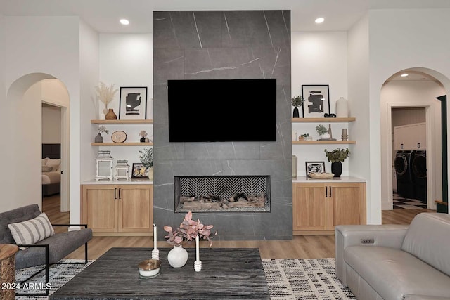 living room with light hardwood / wood-style flooring, a towering ceiling, a tile fireplace, and separate washer and dryer