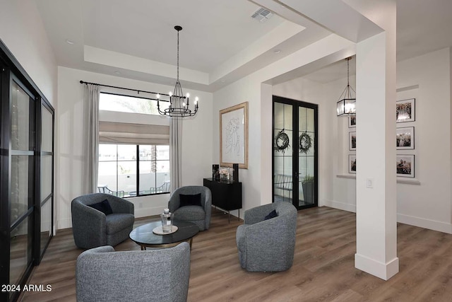 living room with an inviting chandelier, wood-type flooring, and a raised ceiling