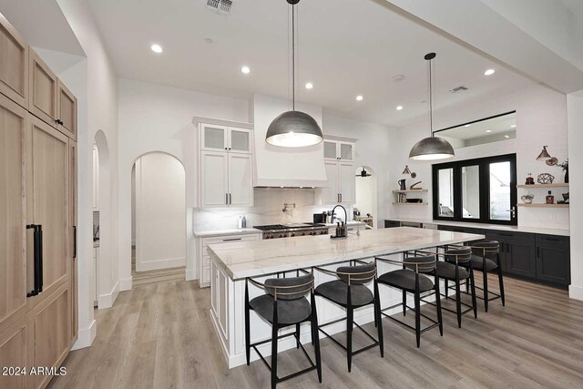 kitchen featuring hanging light fixtures, light stone counters, white cabinets, light wood-type flooring, and a spacious island