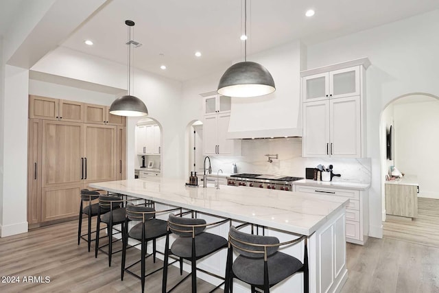 kitchen featuring white cabinetry, decorative light fixtures, light hardwood / wood-style floors, and a large island with sink