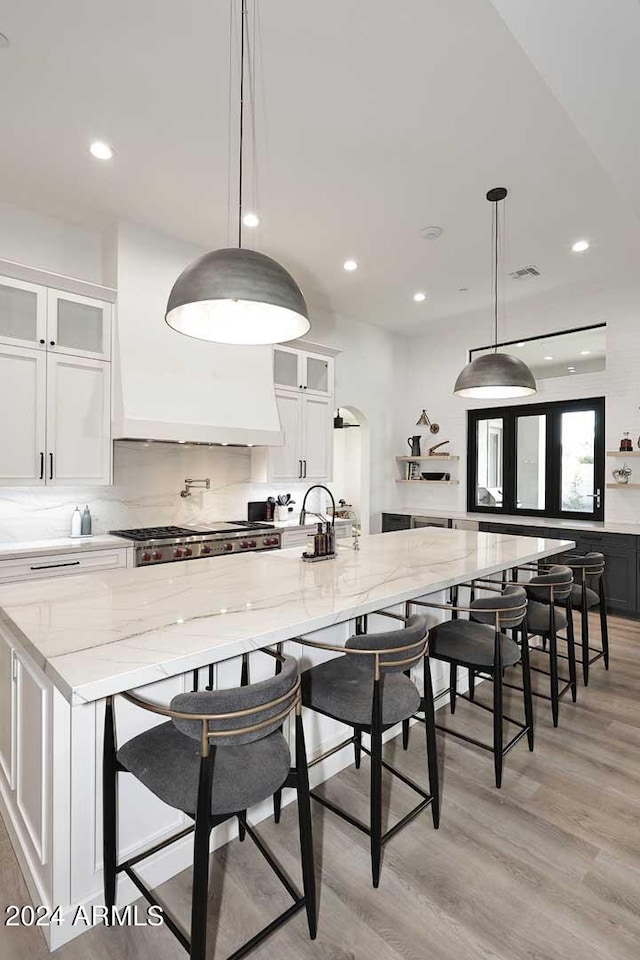 kitchen with light stone counters, light hardwood / wood-style flooring, decorative light fixtures, white cabinetry, and a spacious island