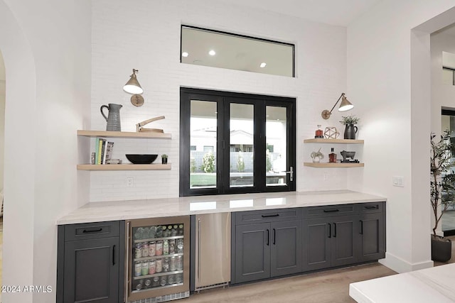 bar with wine cooler, light hardwood / wood-style floors, tasteful backsplash, light stone countertops, and stainless steel fridge