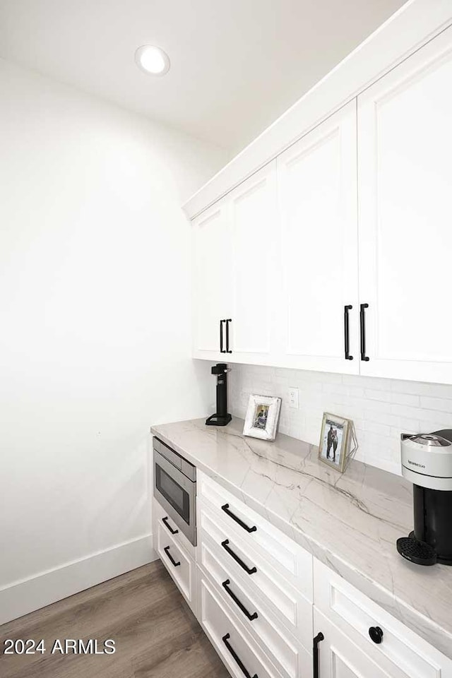 interior space featuring backsplash, stainless steel microwave, and hardwood / wood-style floors