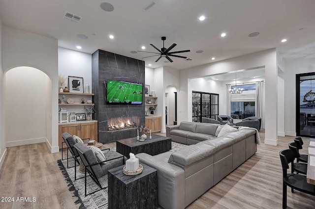 living room featuring ceiling fan with notable chandelier, a tiled fireplace, and light hardwood / wood-style flooring