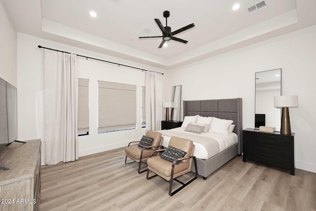 bedroom featuring ceiling fan, a tray ceiling, and light wood-type flooring