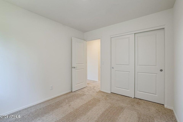 unfurnished bedroom with light colored carpet, baseboards, and a closet