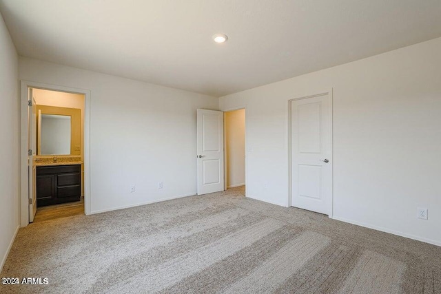 unfurnished bedroom with light colored carpet, ensuite bath, baseboards, and a sink