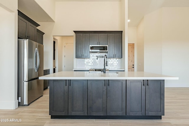 kitchen featuring appliances with stainless steel finishes, a kitchen island with sink, sink, and light hardwood / wood-style flooring