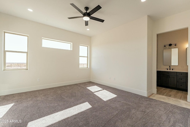 unfurnished bedroom with ensuite bathroom, sink, light colored carpet, and ceiling fan