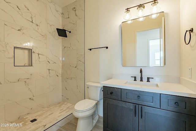 bathroom with a tile shower, vanity, and toilet