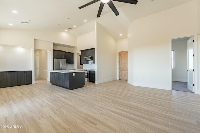 kitchen featuring appliances with stainless steel finishes, high vaulted ceiling, ceiling fan, a center island with sink, and light wood-type flooring