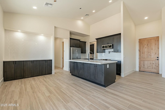 kitchen with tasteful backsplash, appliances with stainless steel finishes, a center island with sink, and light wood-type flooring