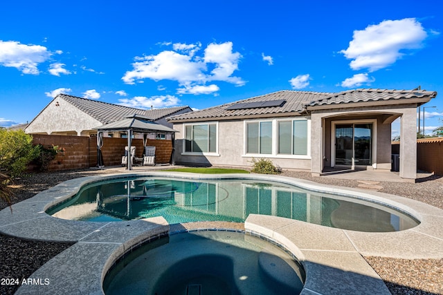 back of house featuring a gazebo, a patio, a pool with hot tub, and solar panels