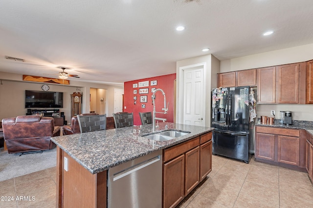 kitchen with dishwasher, sink, black fridge, a center island with sink, and light tile patterned floors