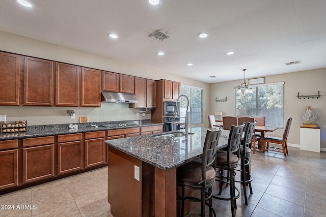 kitchen featuring a kitchen island with sink, black appliances, hanging light fixtures, light tile patterned floors, and a notable chandelier