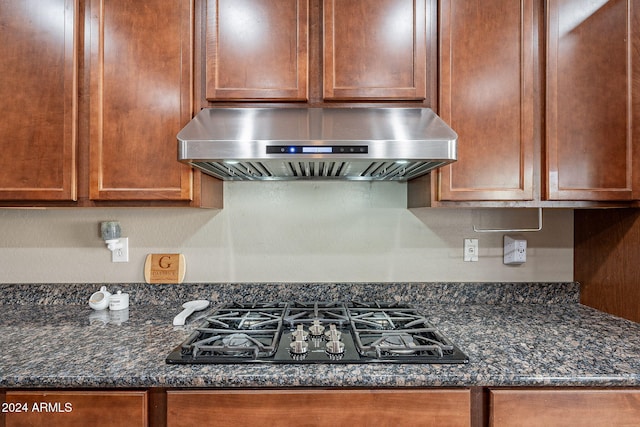 kitchen featuring dark stone countertops, wall chimney exhaust hood, and stainless steel gas cooktop