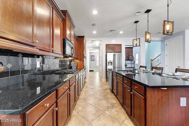 kitchen with a sink, visible vents, black appliances, tasteful backsplash, and a center island with sink