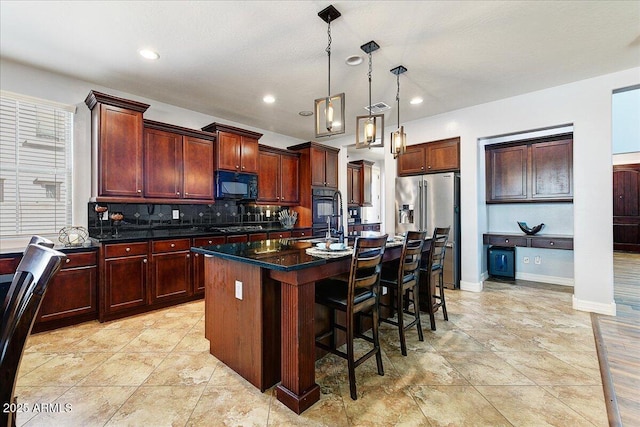 kitchen with black microwave, high quality fridge, a kitchen island with sink, a breakfast bar, and backsplash