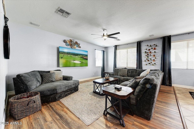 living room with a textured ceiling, wood finished floors, visible vents, and baseboards